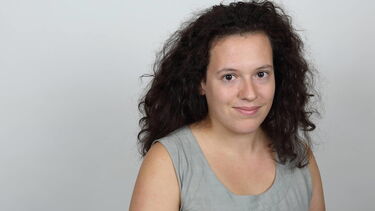 A photo of a woman with curly hair, standing in front of a grey background