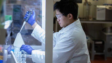A researcher using a pipette in a fume cupboard 