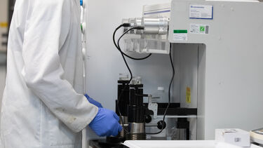 A researcher wearing a white lab coat and PPE in a lab