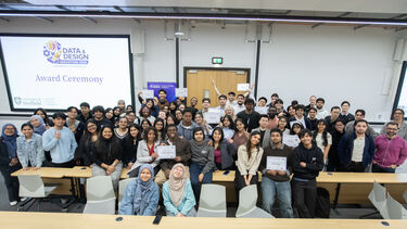 A group of students and staff standing in a lecture theatre, some holding certificates