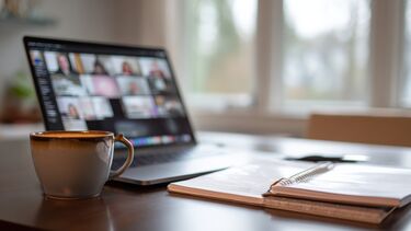An image showing an open laptop showing an online meeting in progress, with a cup of coffee on a desk