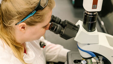 A researcher looking down a microscope 