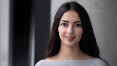 Hazal has long dark hair and dark eyes. She wears a grey jumper.