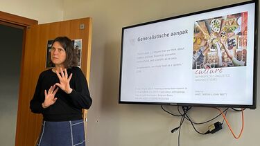 Dr Truus De Wilde standing in  front of a screen clearly talking to a group. The slide reads: generalist approach