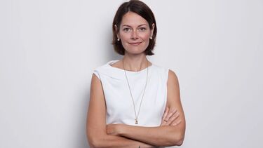 A woman standing against a white background, smiling, with her arms folded