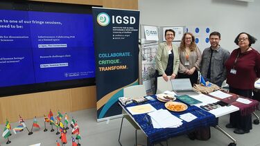 Four people stand next to an IGSD banner, behind a table