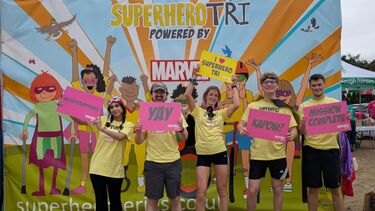 Five people smiling and holding signs in front of a colourful; superhero themed banner