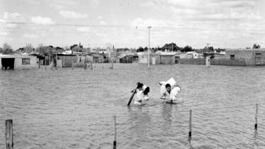 Two people carrying bundles through a flooded town