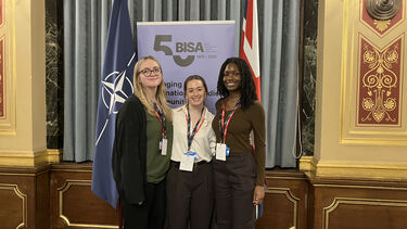 Three students posing in front of flags at the model NATO