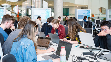 A group of computer science students in a room working on laptops