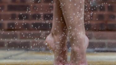 Feet with painted toenails are dancing in the rain with a brick wall in the background