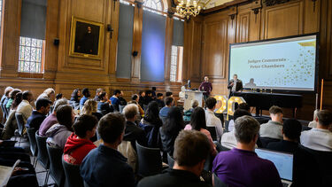 Room full presentation of awards in old room with decoration lights and audience looking at speaker