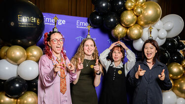 Students smiling in front of photo booth with trophies on their head 