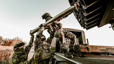 Soldiers in camouflage uniforms loading artillery equipment during a military field operation