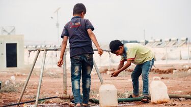 Two refugee boys collect water in plastic bottles