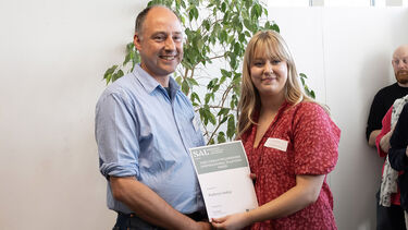 Student showing certificate and smiling with employer sponsor