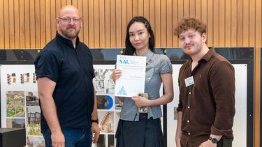 Student awarded prize on stage with two sponsors 