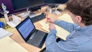 Ed sits at a laptop, making notes on a pad of paper