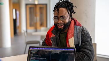 A student sits in an internal study space and laughs with someone sat off camera. There is a laptop in the foreground.