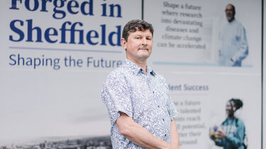 Richard Cooper stood in front of a poster 'Forged in Sheffield' on the window of The Diamond Building.