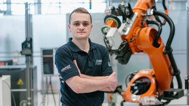 Sean Delaney stood in front of an orange robotic machine arm.