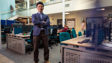 Dr Leslie Ing stands arms crossed in a busy office space