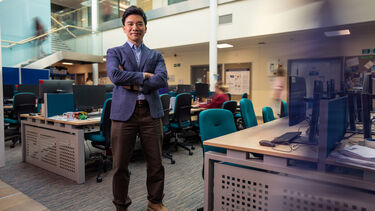 Dr Leslie Ing stands arms crossed in a busy office space