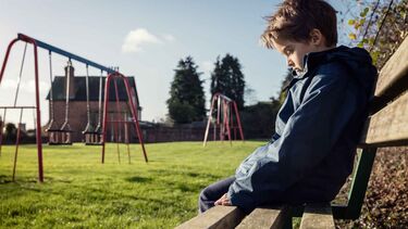 Child alone sitting on a bench with swings in the background