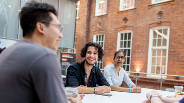 Three students sit at a table in the Heartspace and laugh with one another