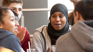 A group of four students sit around a table talking.