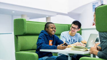 Three students sit in a booth and talk with one another