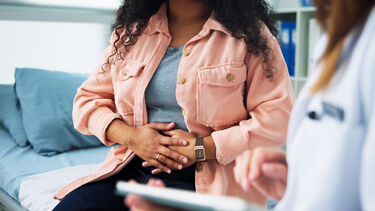Woman holding her stomach while speaking to a doctor.
