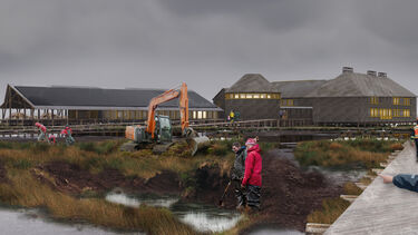 People standing by marshland with an orange digger in front of a collection of buildings
