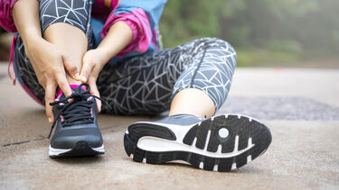A woman sitting down on the road holding her ankle after sustaining an injury while jogging