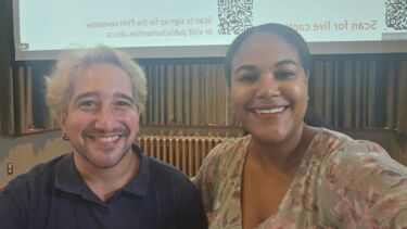 Antonios and Nadena are smiling at the camera and they are in front of a screen projecting the introductory slide
