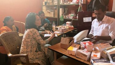 A group of people sat at tables, with boxes of medication 