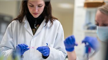 Student in lab coat looking at slides.