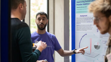 A Grantham Scholar points to his research poster while talking to a member of the public
