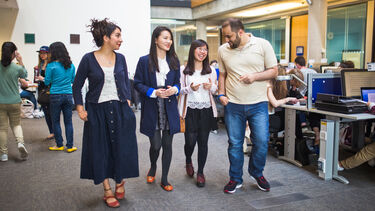 Four students walk together through an indoor study space, talking and smiling.