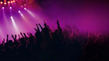A stylised image of a live concert where the sillouetted crowd have their hands in the air