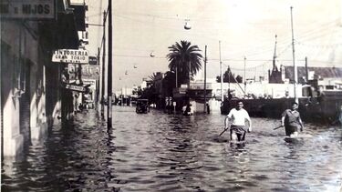 A black and white photo of the 1967 flood in Buenos Aires showing two men wading down a flooded street with water up to their waist
