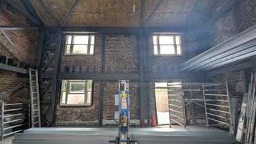 The inside of a small brick building, the height of 2 floors but with no first floor installed.  3 windows and 1 doorway along the back wall.  Metal frame visible.