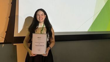 A woman standing, holding a certificate in front of a screen.