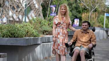 Image of Tom Davies who is living with MND in his wheelchair alongside his partner Alex