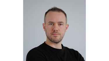 A head and shoulders portrait of a white man wearing a dark top