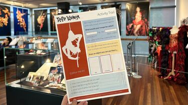 A hand holds a colourful activity sheet in an exhibition space. 