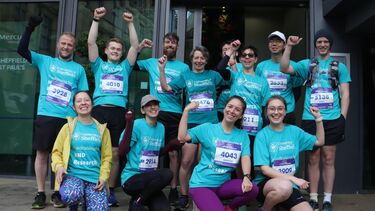 A group of people in blue shirts are smiling with their arms raised in the air 