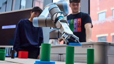 Two children in the background look at a robotic arm demonstration