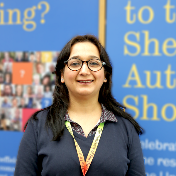 Profile picture of Aarti stands in front of the Author's Showcase at Western Bank Library