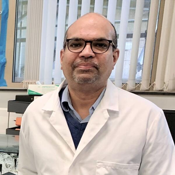 Profile picture of Manoj Menon in a lab standing next to some scientific equipment